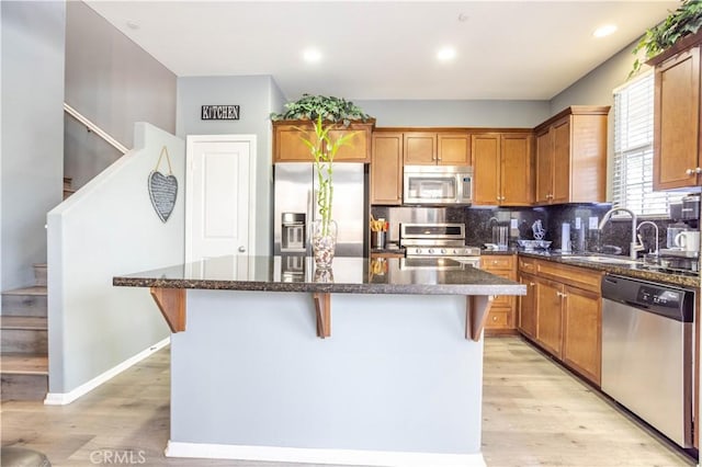 kitchen with appliances with stainless steel finishes, sink, a kitchen bar, dark stone counters, and a center island