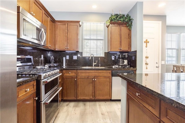 kitchen with sink, light hardwood / wood-style flooring, appliances with stainless steel finishes, dark stone countertops, and backsplash