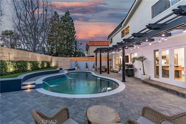 pool at dusk with area for grilling, a pergola, a patio area, and french doors