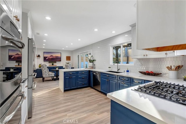 kitchen featuring blue cabinetry, sink, light wood-type flooring, kitchen peninsula, and stainless steel appliances