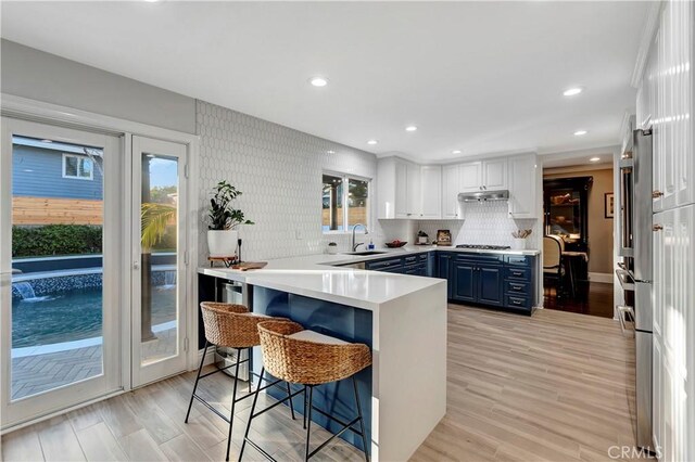 kitchen featuring white cabinetry, sink, a breakfast bar area, kitchen peninsula, and blue cabinetry