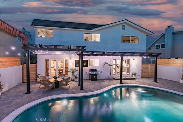 back house at dusk featuring a pergola and a patio area