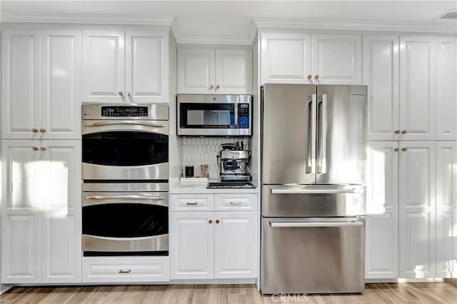 kitchen with decorative backsplash, light hardwood / wood-style flooring, white cabinets, and appliances with stainless steel finishes