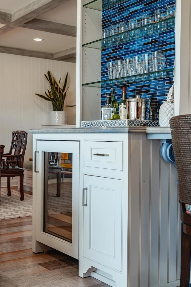 bar featuring wine cooler, beamed ceiling, wood-type flooring, and white cabinets