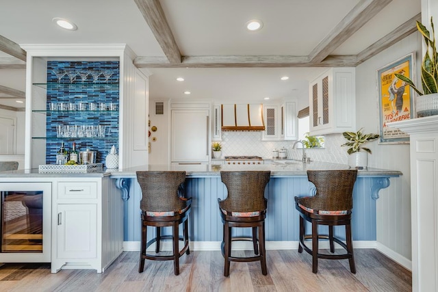 bar featuring sink, white cabinets, beverage cooler, beam ceiling, and light hardwood / wood-style flooring