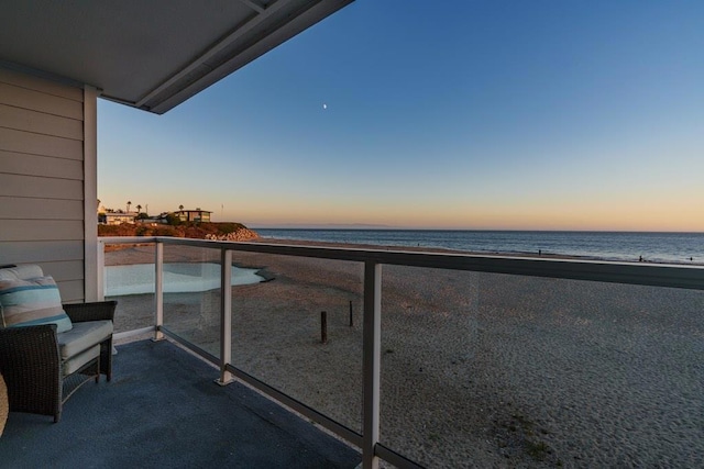 balcony at dusk featuring a water view and a view of the beach