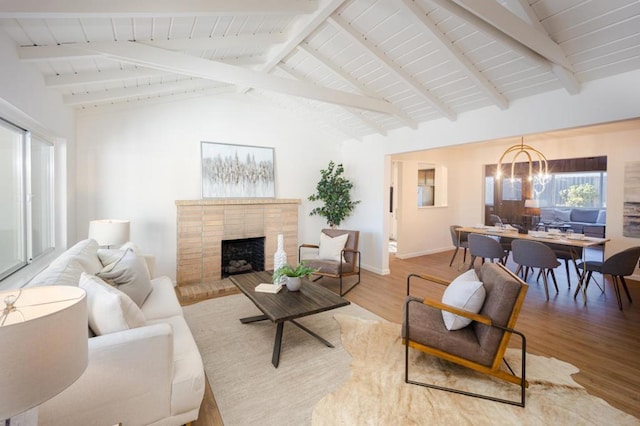 living room featuring wood-type flooring, a brick fireplace, vaulted ceiling with beams, and a chandelier