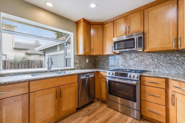 kitchen featuring sink, tasteful backsplash, light wood-type flooring, appliances with stainless steel finishes, and light stone countertops