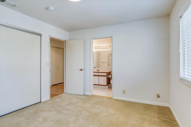 unfurnished bedroom featuring ensuite bathroom, sink, light carpet, and a closet