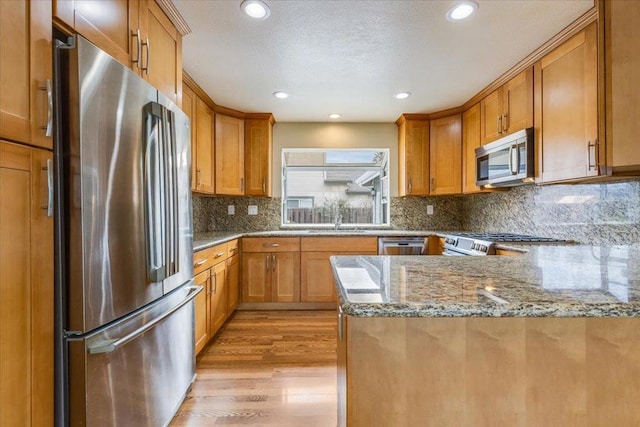 kitchen with light stone counters, tasteful backsplash, light hardwood / wood-style flooring, kitchen peninsula, and stainless steel appliances