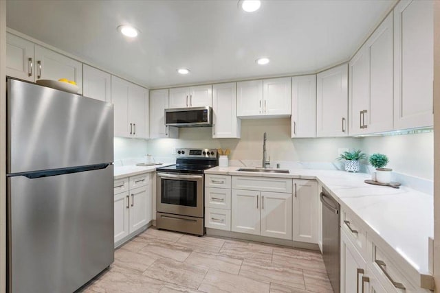 kitchen with appliances with stainless steel finishes, light stone countertops, sink, and white cabinets