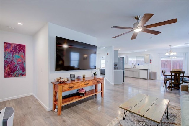 living room with ceiling fan with notable chandelier and light wood-type flooring