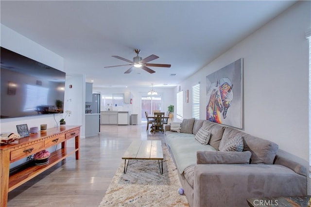 living room featuring ceiling fan with notable chandelier and light hardwood / wood-style floors