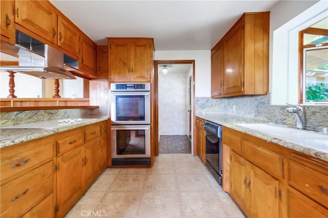 kitchen featuring light stone counters, double oven, sink, and dishwasher