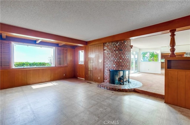 unfurnished living room featuring a healthy amount of sunlight, a textured ceiling, a fireplace, and wood walls