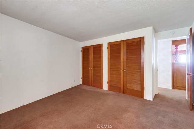 unfurnished bedroom featuring two closets, a textured ceiling, and carpet