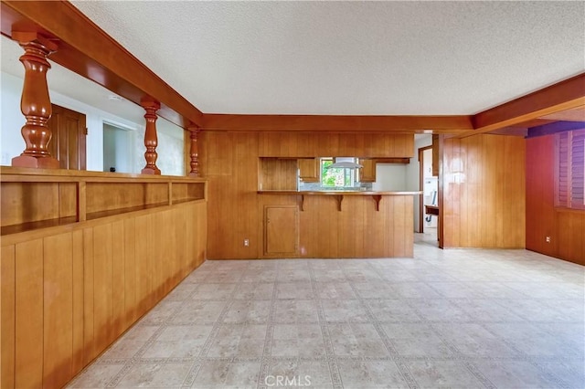 interior space featuring wood walls, a kitchen breakfast bar, kitchen peninsula, wall chimney range hood, and a textured ceiling