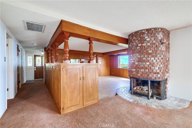 interior space with a brick fireplace, light colored carpet, a textured ceiling, and kitchen peninsula