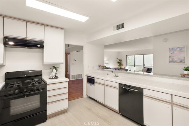 kitchen with tile countertops, sink, white cabinets, light hardwood / wood-style floors, and black appliances