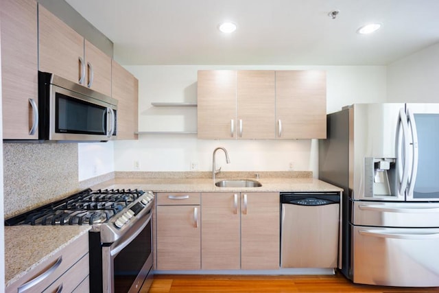 kitchen featuring stainless steel appliances, light brown cabinetry, sink, and light stone countertops