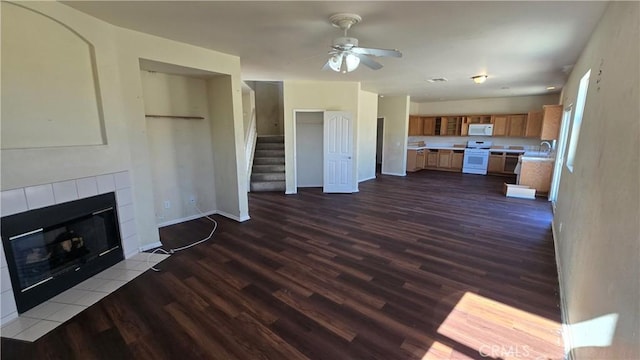 unfurnished living room featuring a tiled fireplace, dark hardwood / wood-style floors, sink, and ceiling fan