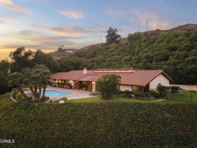 back house at dusk featuring a fenced in pool, a patio, a mountain view, and a yard