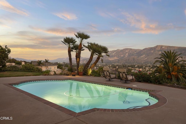 pool at dusk featuring a patio and a mountain view