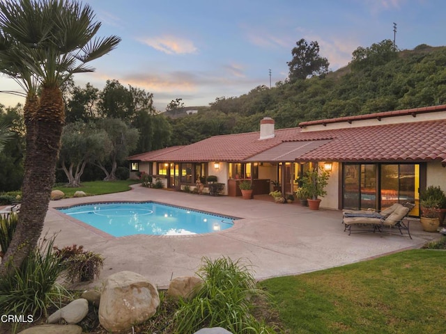 pool at dusk with a patio and a yard