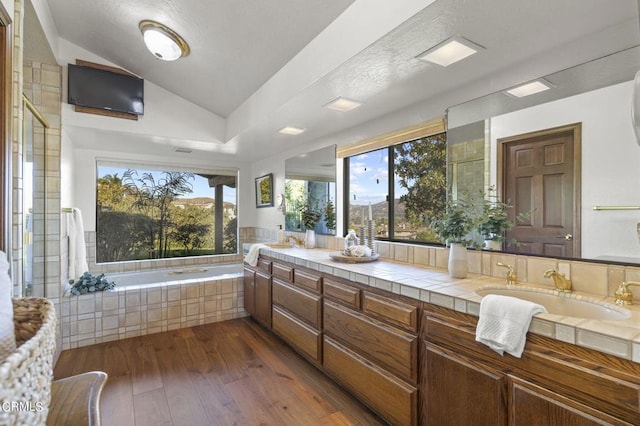 bathroom with vanity, tiled tub, vaulted ceiling, and wood-type flooring