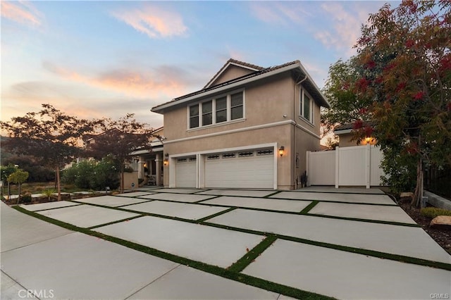 view of front facade featuring stucco siding, driveway, an attached garage, and fence