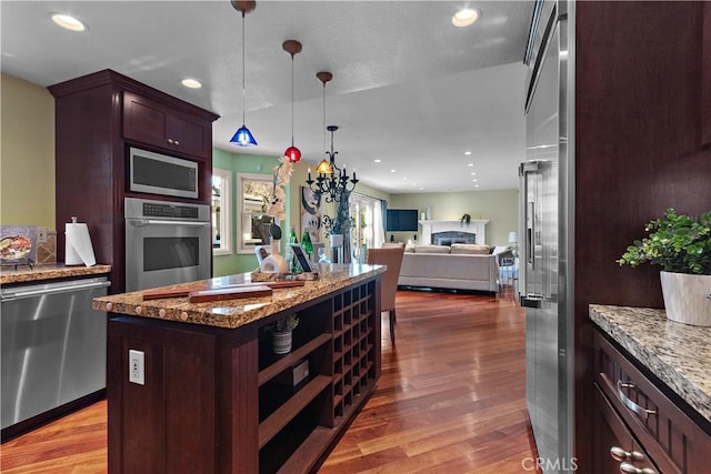 kitchen featuring wood finished floors, a fireplace, appliances with stainless steel finishes, pendant lighting, and open floor plan