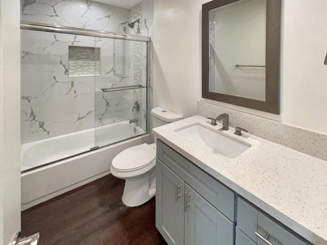 full bathroom with hardwood / wood-style flooring, enclosed tub / shower combo, vanity, and toilet