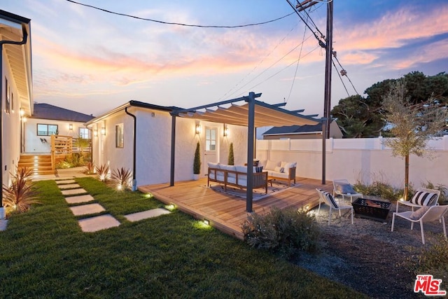 back house at dusk featuring a lawn, a wooden deck, an outdoor living space with a fire pit, and a pergola