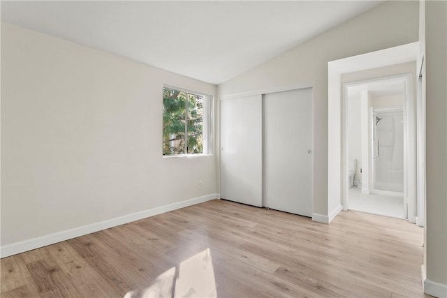 unfurnished bedroom featuring vaulted ceiling, a closet, and light hardwood / wood-style flooring