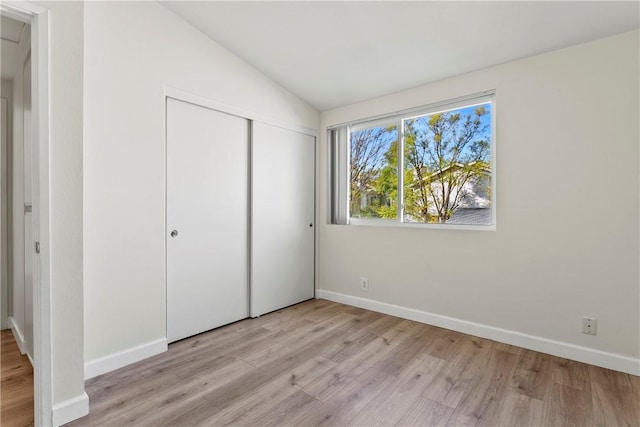 unfurnished bedroom featuring lofted ceiling, a closet, and light wood-type flooring