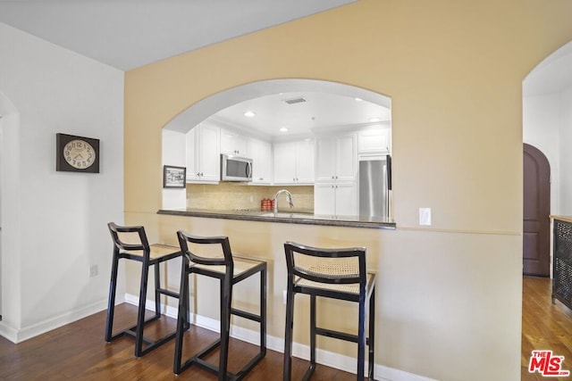 kitchen with white cabinetry, a kitchen breakfast bar, kitchen peninsula, stainless steel appliances, and dark wood-type flooring