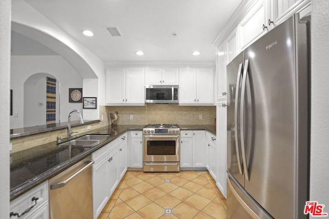 kitchen with appliances with stainless steel finishes, sink, dark stone countertops, white cabinets, and light tile patterned floors