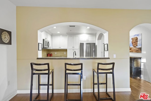 kitchen with stainless steel appliances, white cabinets, a kitchen bar, dark hardwood / wood-style flooring, and kitchen peninsula