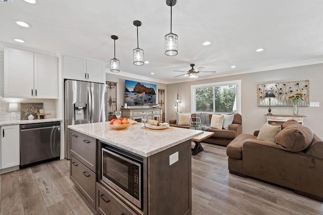 kitchen featuring hanging light fixtures, ornamental molding, stainless steel appliances, and white cabinets