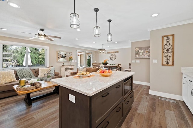 kitchen with dark brown cabinetry, hanging light fixtures, stainless steel microwave, and a healthy amount of sunlight