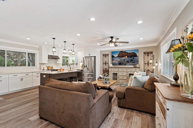 living room featuring crown molding, sink, ceiling fan, and light wood-type flooring