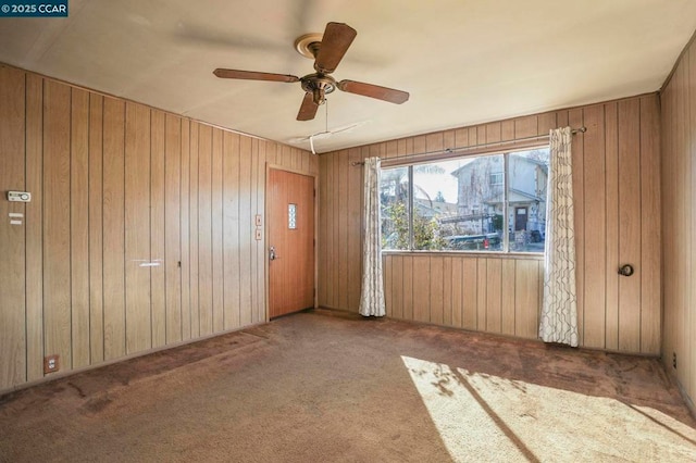 empty room featuring carpet floors, ceiling fan, and wood walls