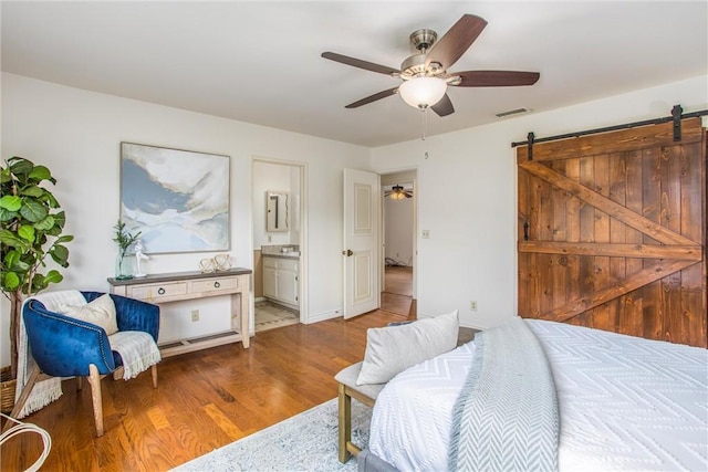 bedroom with ceiling fan, a barn door, light hardwood / wood-style floors, and ensuite bath