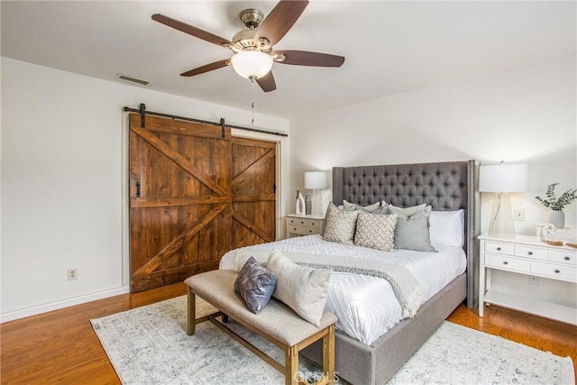 bedroom with wood-type flooring, a barn door, and ceiling fan