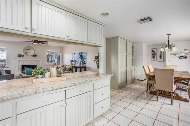 kitchen featuring light tile patterned flooring, pendant lighting, a fireplace, light stone countertops, and ceiling fan with notable chandelier