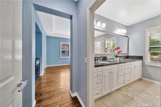 full bathroom featuring double vanity, wood finished floors, baseboards, and a sink