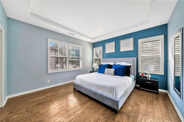 bedroom with visible vents, a raised ceiling, baseboards, and hardwood / wood-style flooring