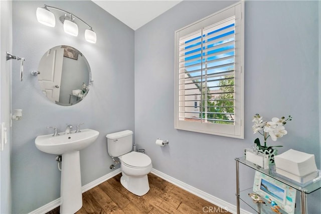 half bath featuring toilet, wood finished floors, baseboards, and a sink