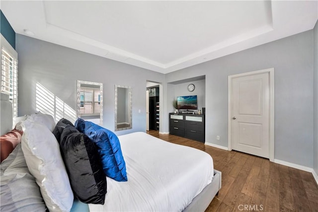 bedroom featuring a tray ceiling, baseboards, and wood-type flooring