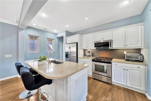 kitchen with a sink, backsplash, stainless steel appliances, wood-type flooring, and a toaster